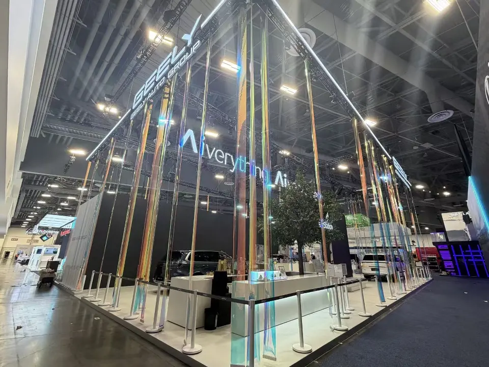 Side view of the Geely stand with iridescent hanging strips, Aiverything lettering and long white welcome counter
